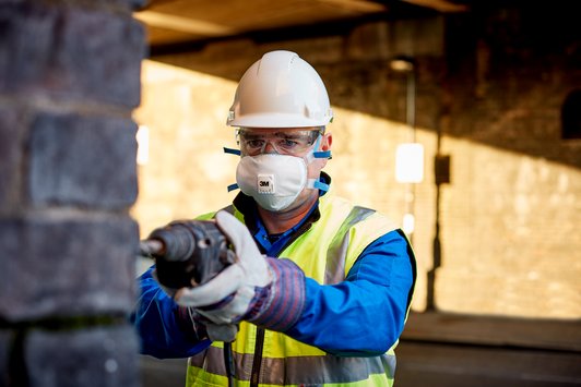 Bouwvakker met helm, veiligheidsbril en 3M Fijnstofmasker 8825+ dat zijn neus en mond bedekt